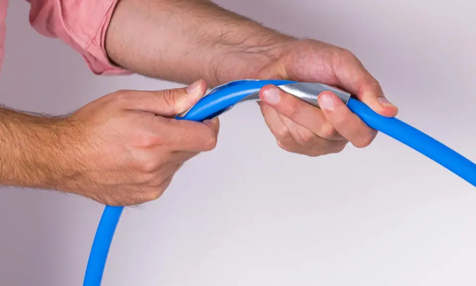 Mains bleues tenant un tuyau bleu avec un outil métallique pour former un coude boule.