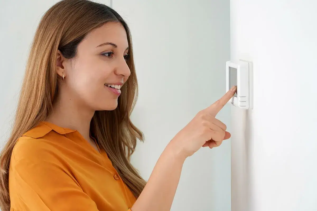 Une femme ajuste son cee thermostat connecté.