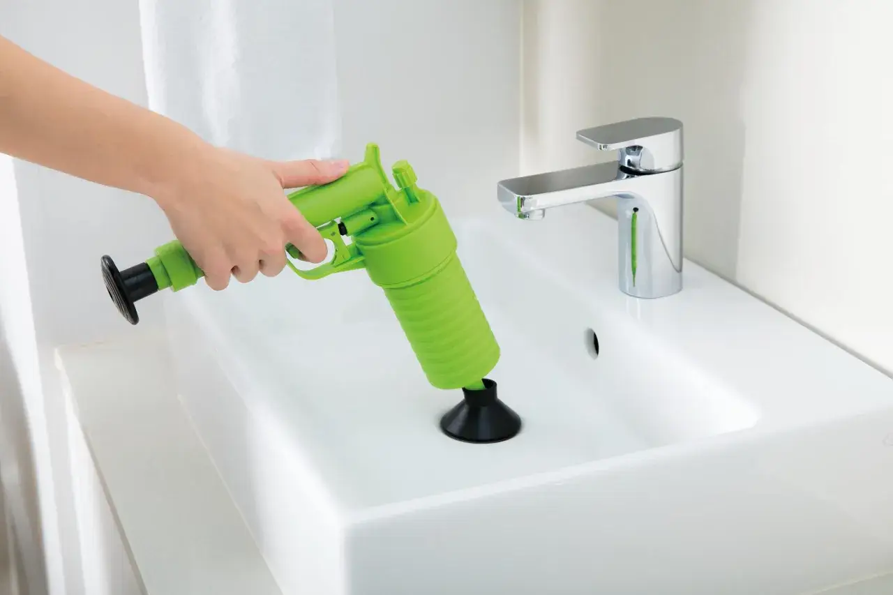 Main verte, un pistolet déboucheur est utilisé pour dégager un lavabo blanc.