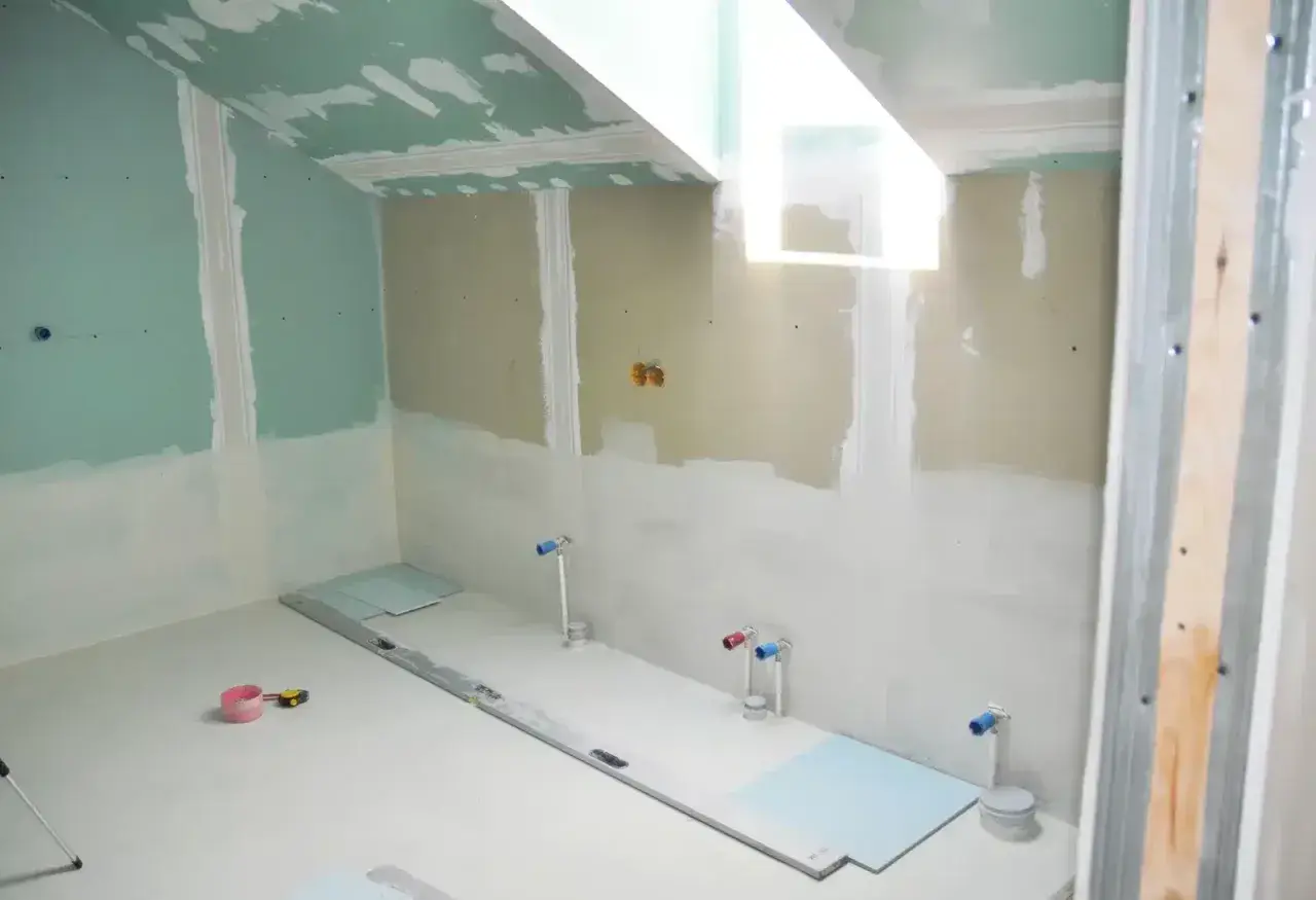 Travaux de finition dans une salle de bain : murs en plaques de plâtre, arrivées d'eau et niveau à bulle au sol. Isolation salle de bain en cours.