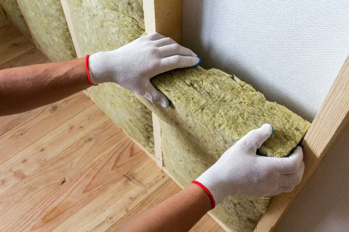 Mains gantées insèrent un isolant dans une structure en bois pour isoler sa maison.