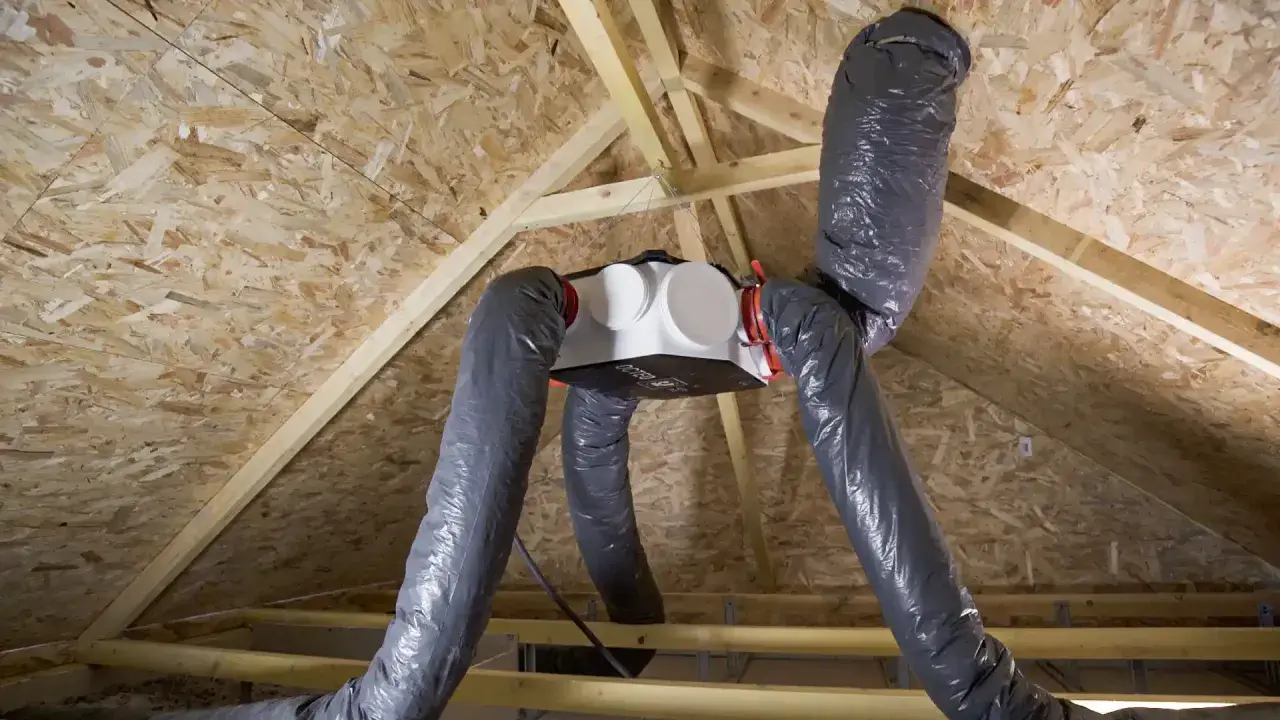 Système VMC double flux installé sous un toit en bois. Les conduits gris souples partent d'une unité centrale blanche. Attention au bruit VMC !