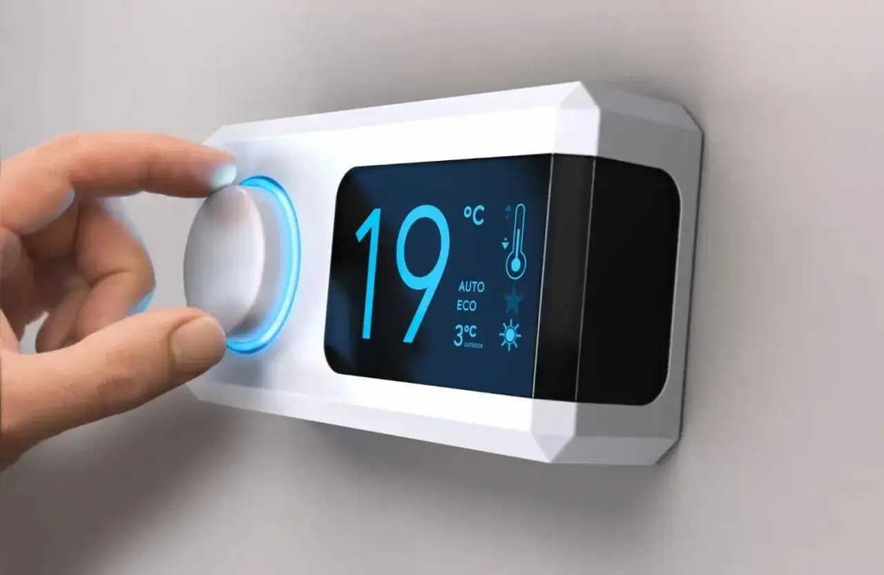 Main d'une personne ajustant le thermostat sur un radiateur électrique, affichant 19°C.