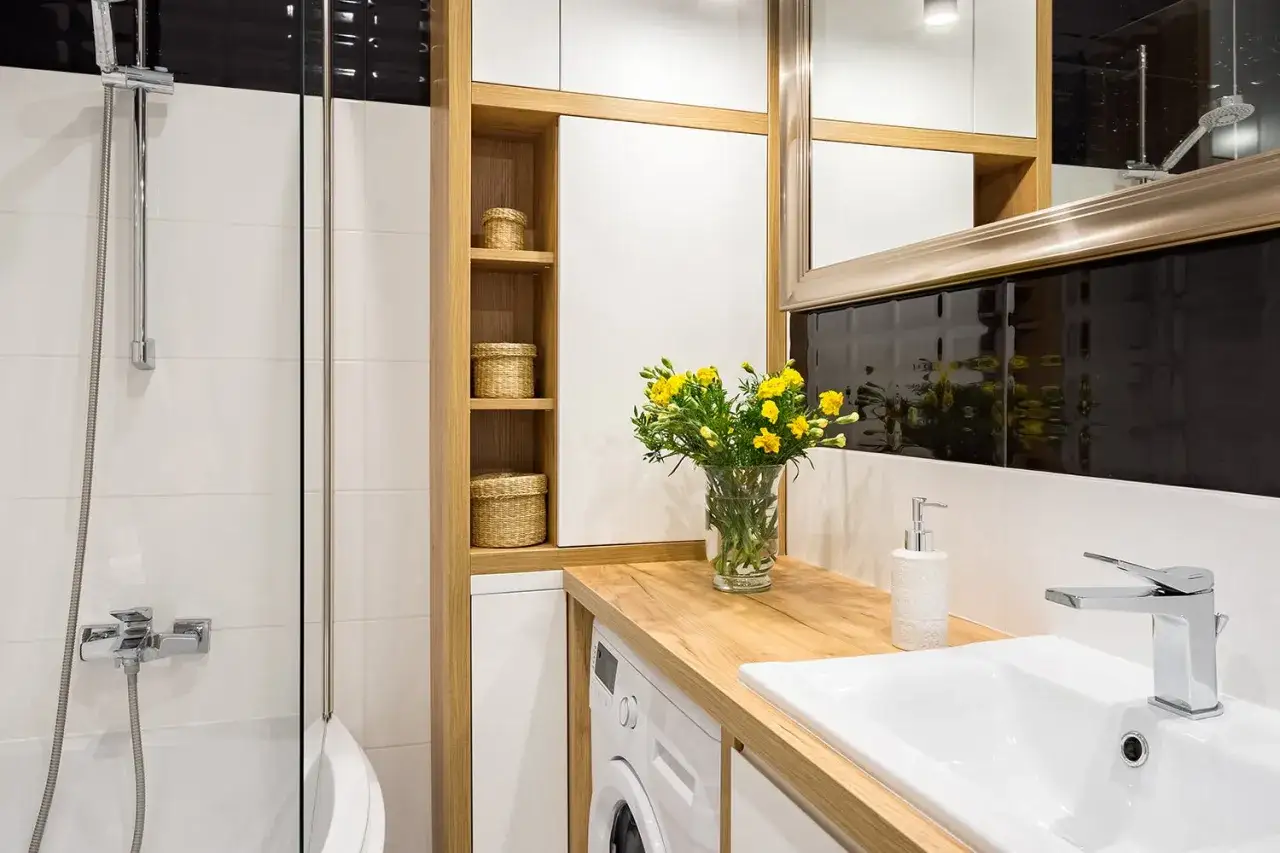 Une petite salle de bain moderne avec une douche, un lavabo, une machine à laver et des paniers en osier sur des étagères en bois.
