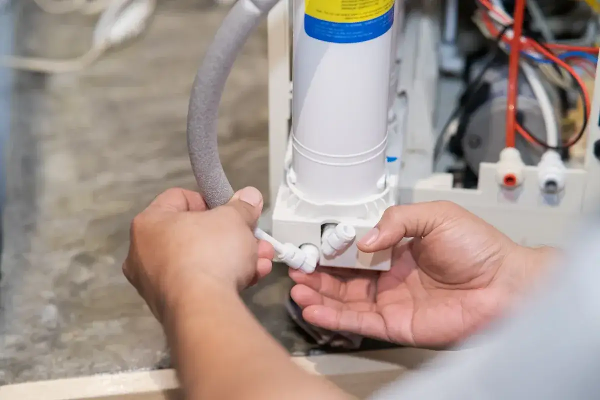 Mains d'un technicien connectant un tuyau à un système de filtration d'eau. Le sel de mon adoucisseur ne fond pas, je vérifie les connexions.
