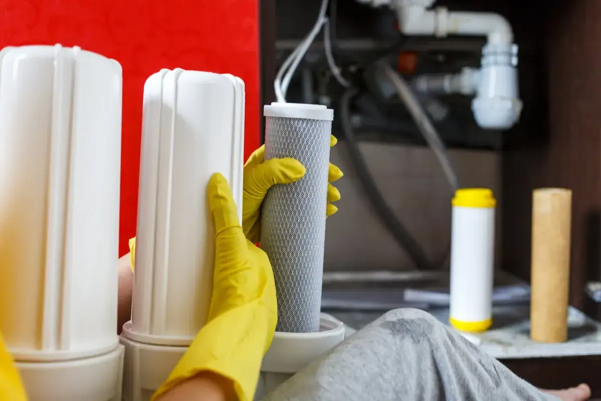 Mains de gant jaune manipulant un filtre à eau, étape du nettoyage résine adoucisseur d'eau.