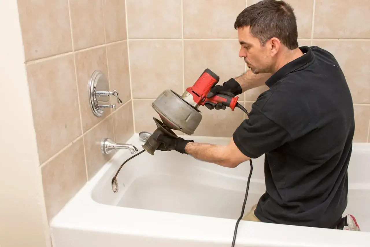 Plombier utilisant une aiguille pour déboucher canalisation dans une baignoire.