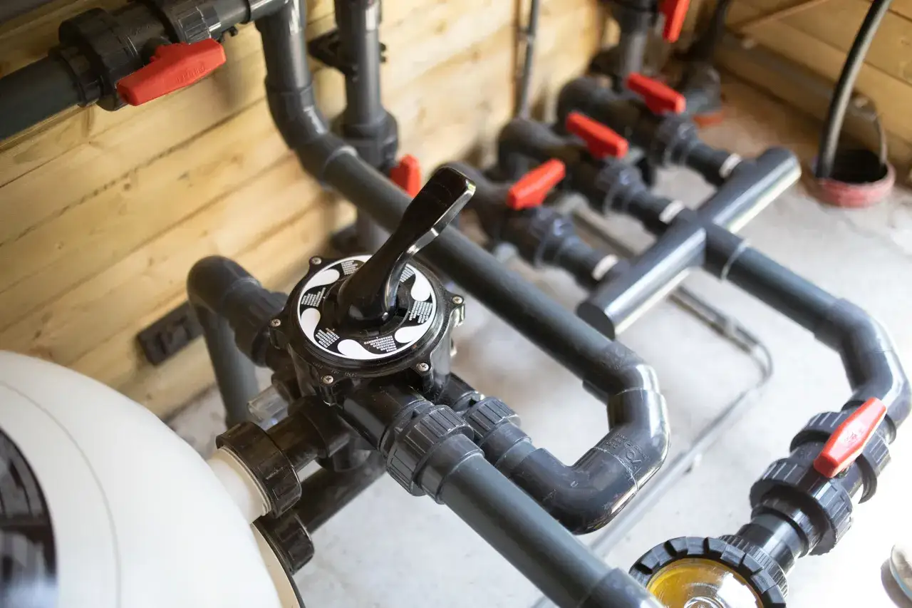 Système de filtration de piscine avec tuyauterie complexe et vannes rouges. Le plan local technique piscine est bien organisé.