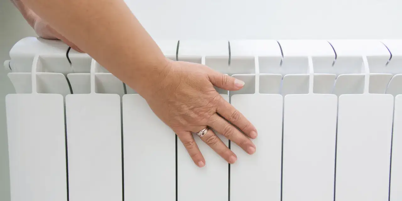 Main posant sa main sur un radiateur blanc, v&eacute;rifiant la temp&eacute;rature hors gel de la maison.
