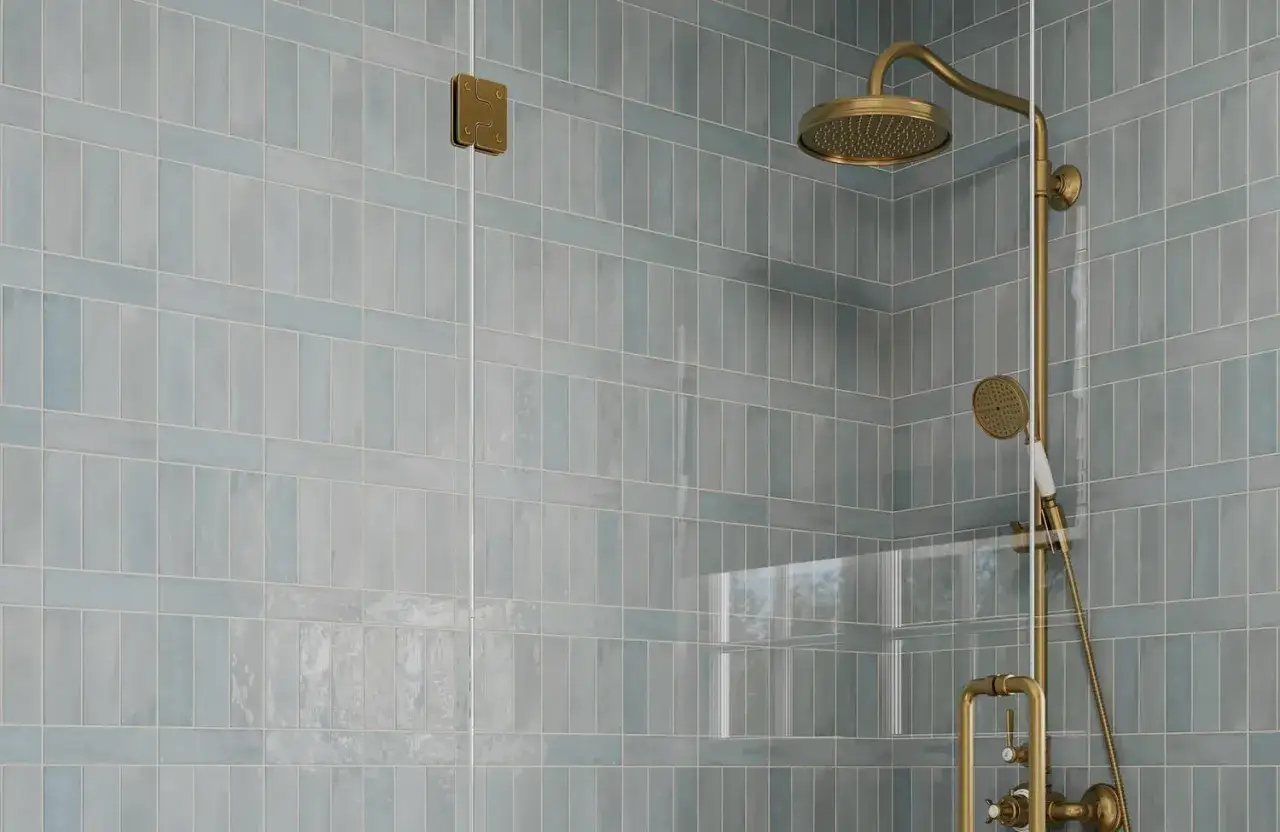 Installation d'une colonne de douche dorée sur un mur carrelé bleu pastel.