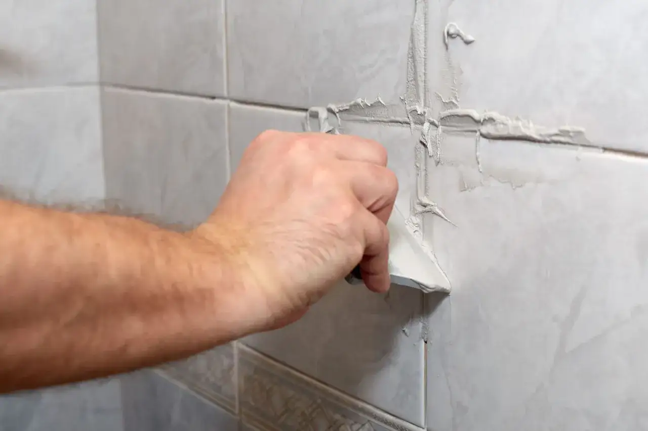 Main d'un bricoleur appliquant du mastic pour refaire joint carrelage.