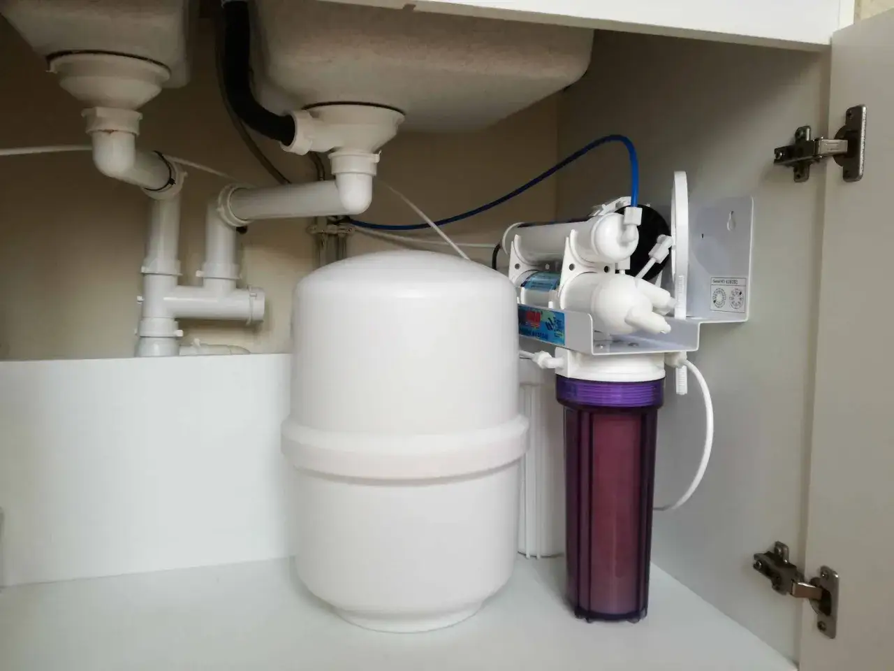 Sous l'évier, un système de filtration d'eau avec un réservoir blanc et un filtre violet. Un problème avec l'adoucisseur Comap ?