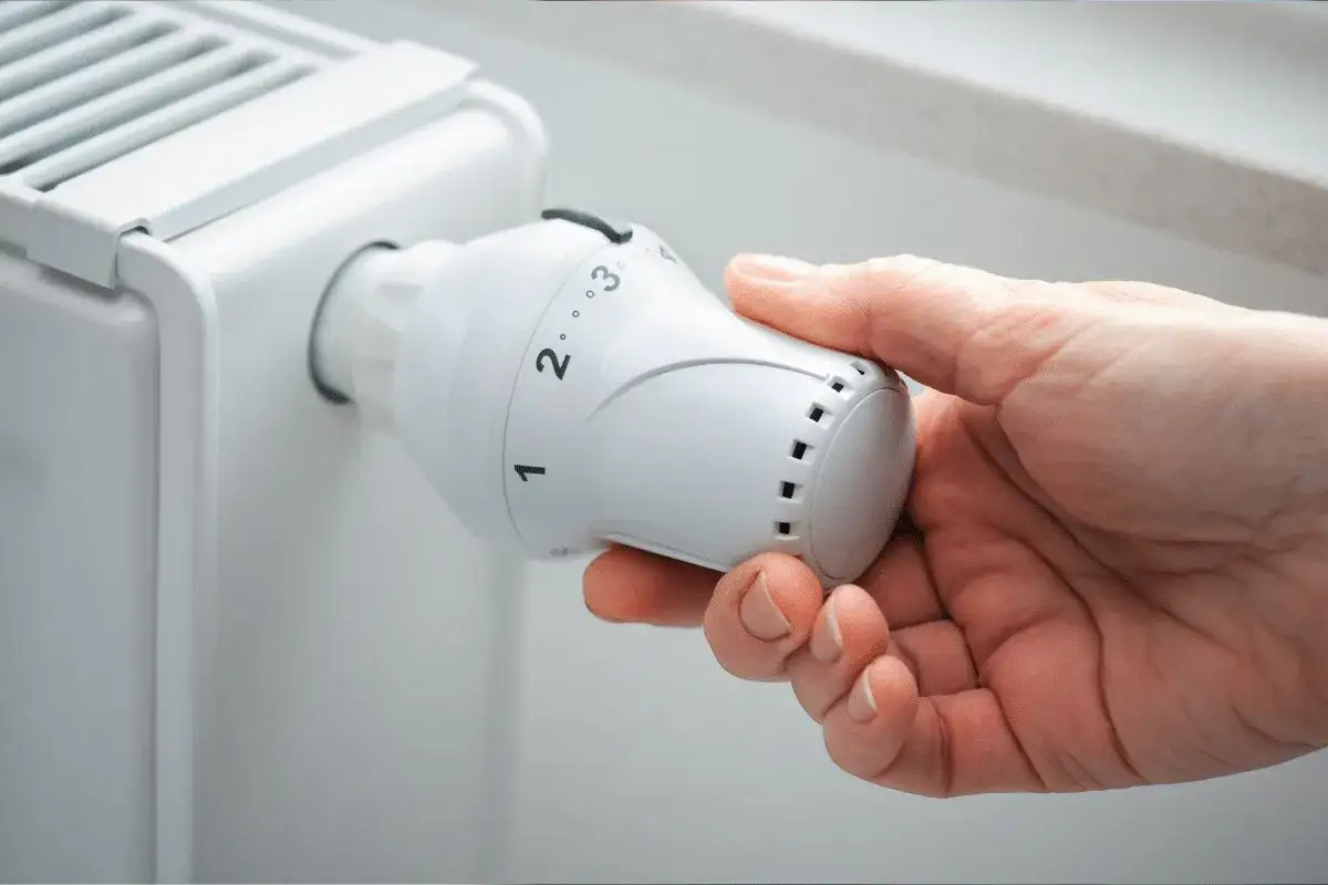 Main tenant ajuste le thermostat d'un radiateur, se demandant s'il faut fermer les radiateurs en été pour économiser de l'énergie.