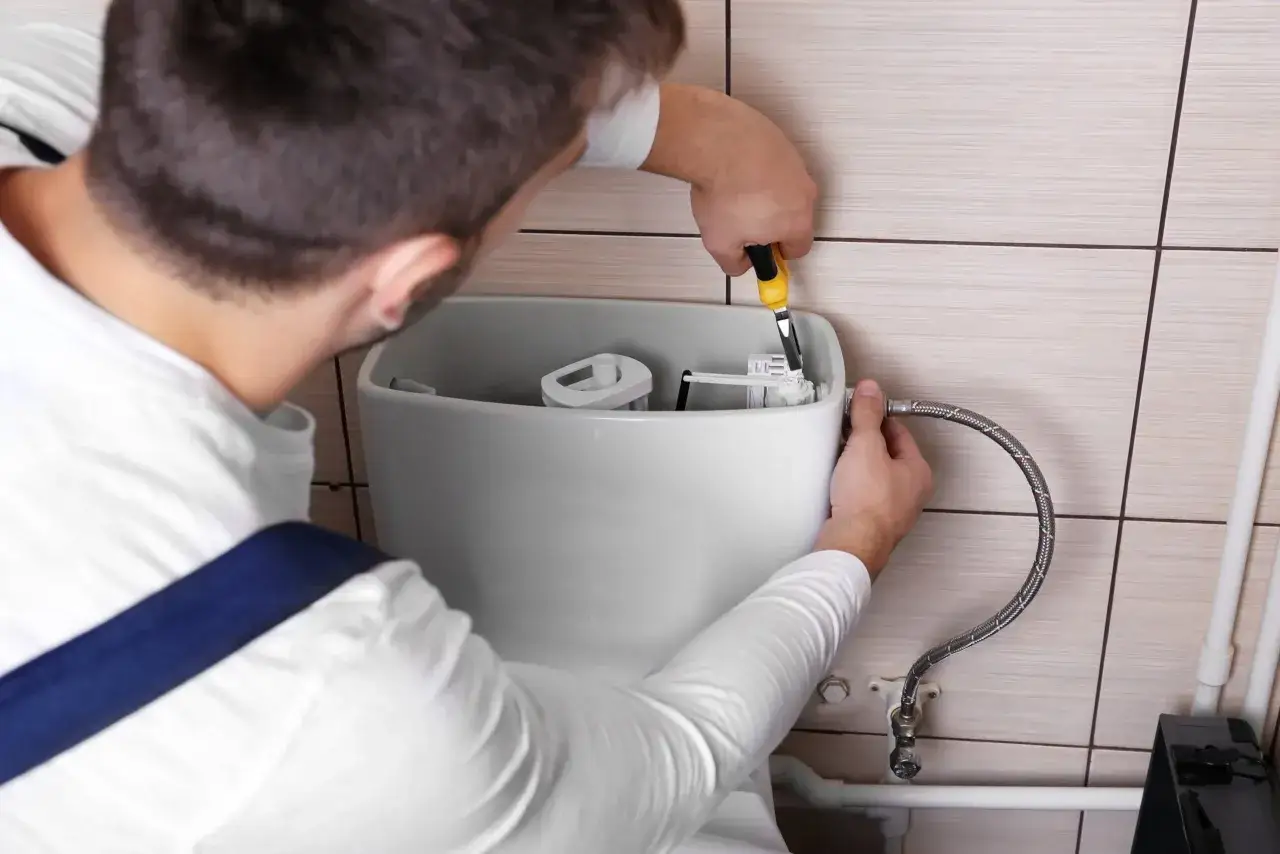 Plombier répare une chasse d'eau qui coule. Il utilise une pince pour ajuster le mécanisme interne.
