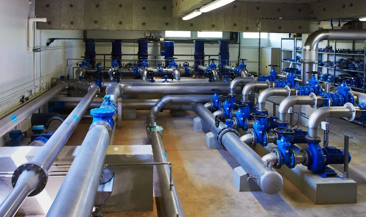 Système de pompage complexe avec tuyauterie en acier inoxydable et pompes bleues, conçu pour éliminer le fer dans l'eau de forage.
