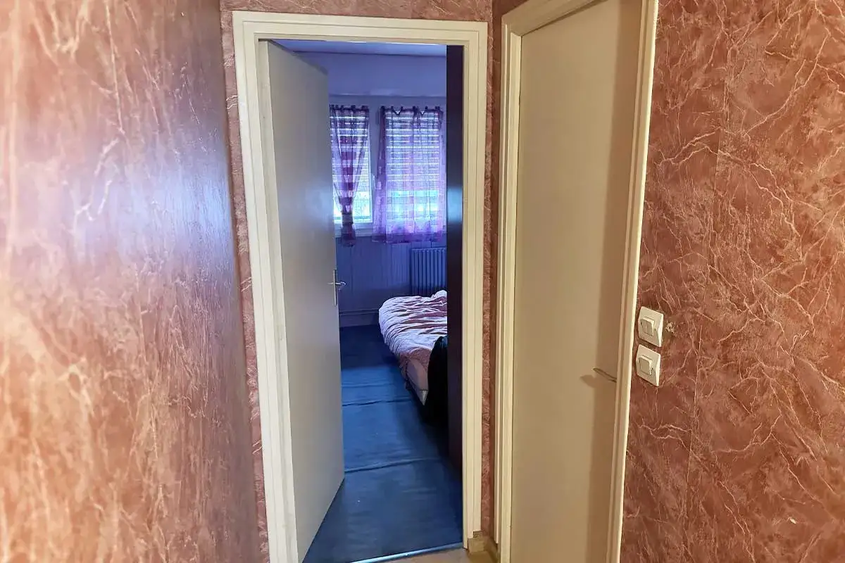 Vue d'un couloir avec un radiateur derrière une porte ouverte menant à une chambre.