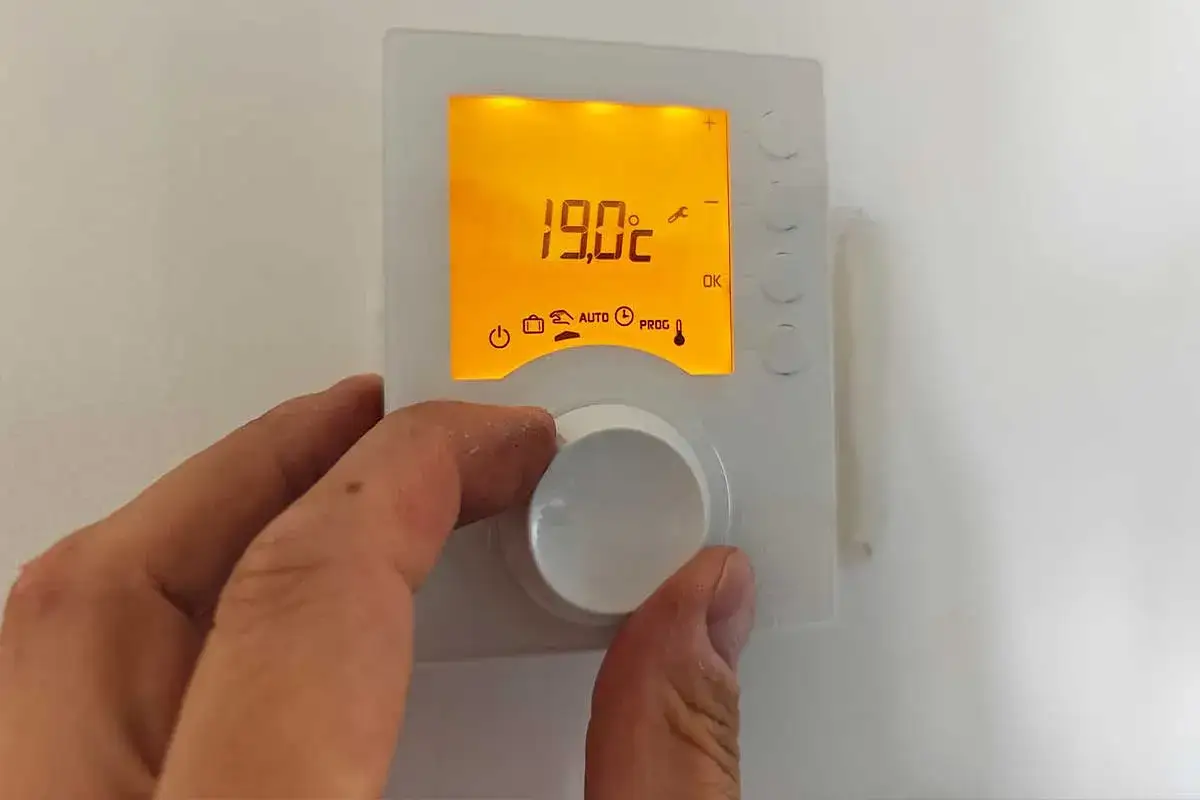 Main tenant ajuste le thermostat pour le chauffage, choisissant entre le mode éco ou confort. L'écran affiche 19.0°C.