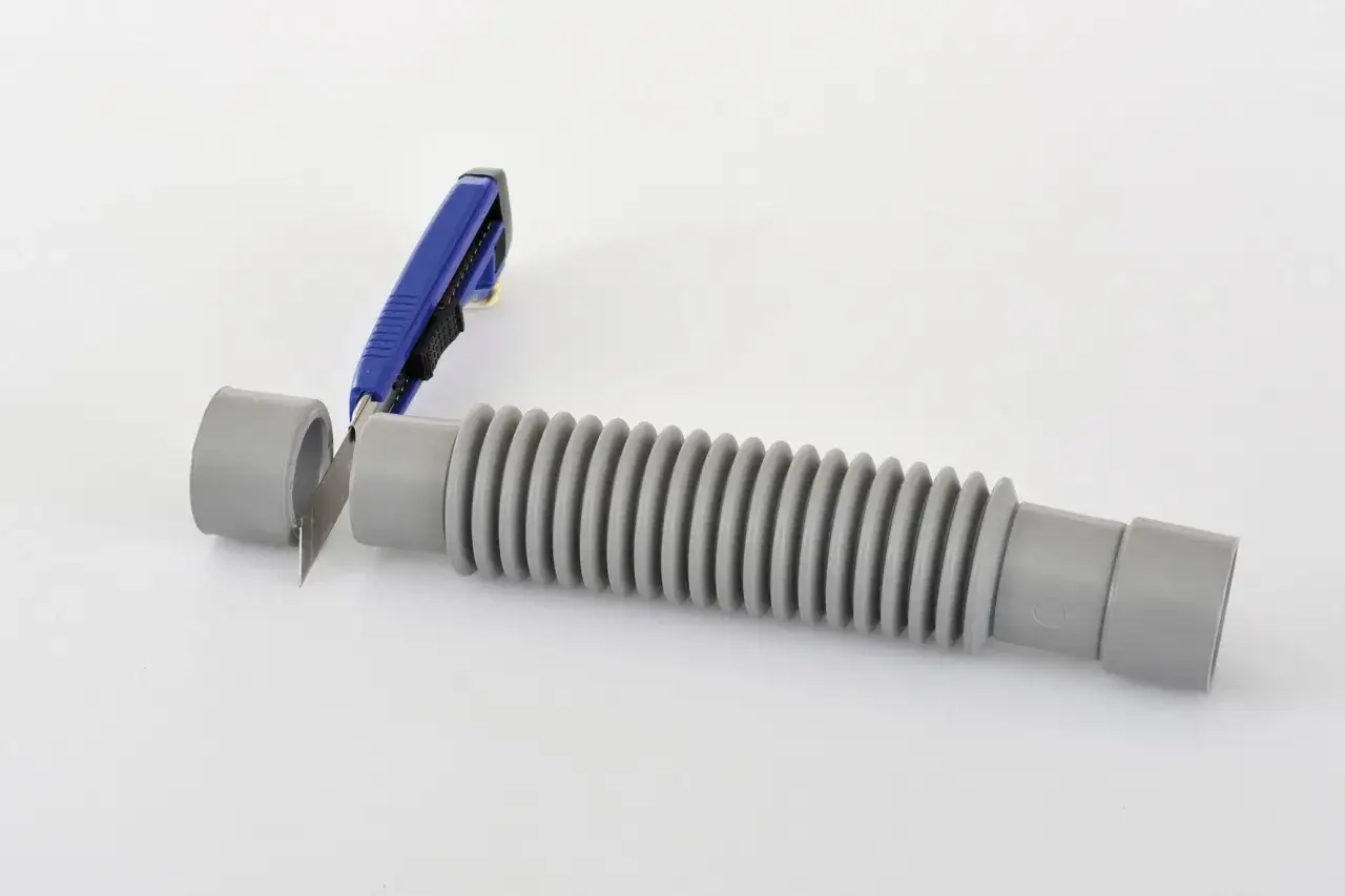 Un cutter bleu coupe un tuyau gris en pvc souple, prêt à être ajusté.