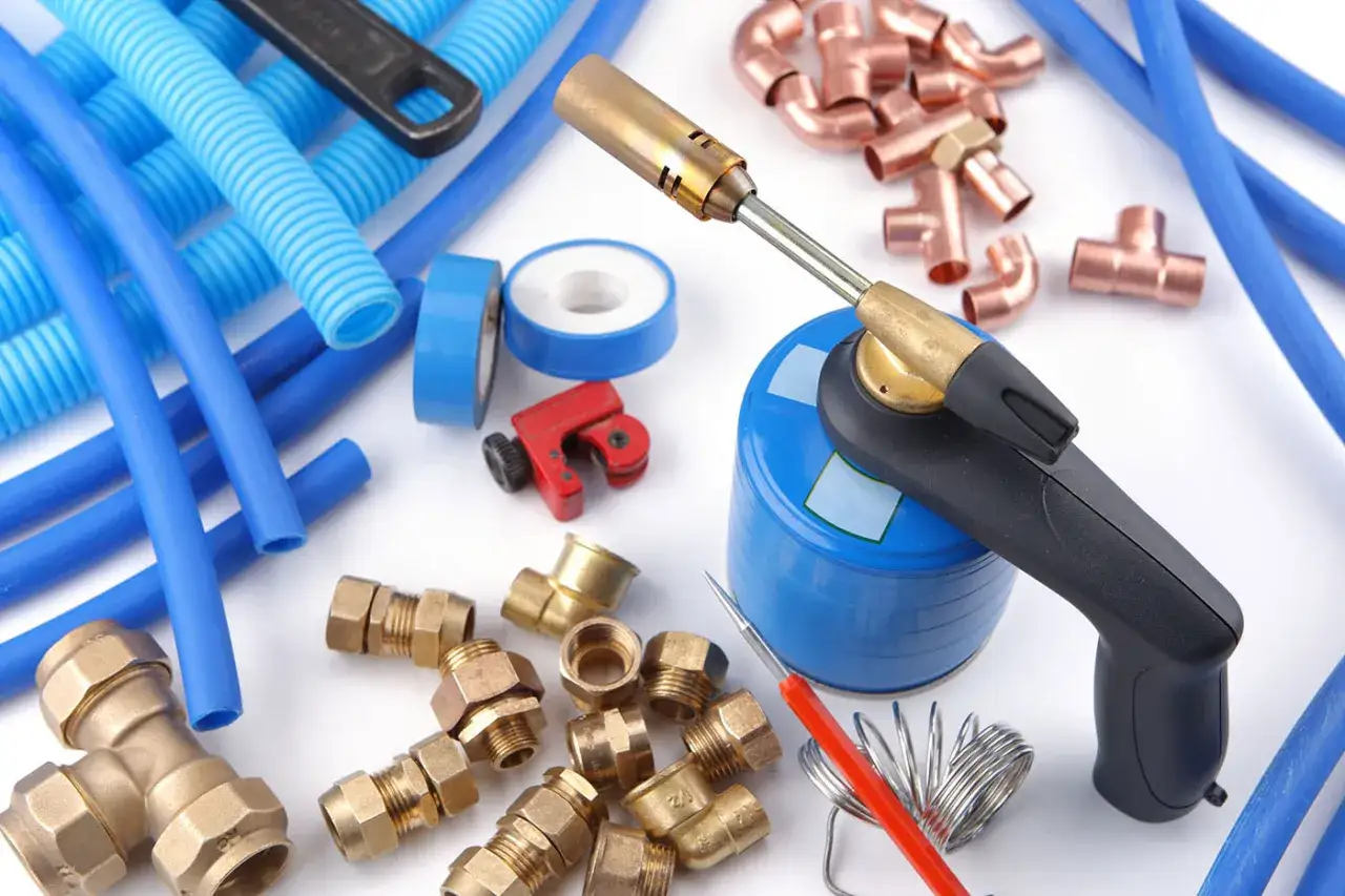Outils de plomberie : chalumeau, raccords en cuivre et laiton, tuyau 12 mm bleu, coupe-tube, ruban de téflon.