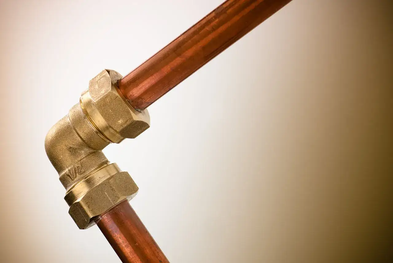Un coude en laiton relie deux tuyaux en cuivre, illustrant une installation de plomberie sans soudure efficace et durable.