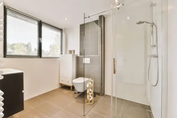 Salle de bain moderne avec une douche italienne, un WC suspendu et un meuble vasque. La lumière naturelle filtre à travers les stores.
