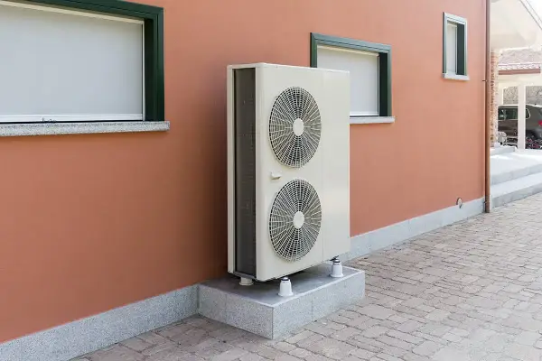 Unité extérieure de pompe à chaleur, avec ses deux ventilateurs, installée sur un socle devant un mur ocre. Le poids de cet appareil assure sa stabilité.