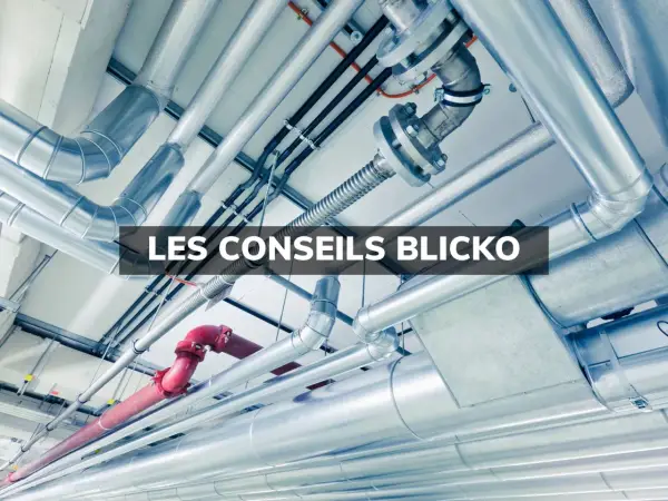 Un réseau complexe de tuyaux argentés et un tuyau rouge, installés au plafond. Ces tuyaux semblent cacher des secrets techniques.