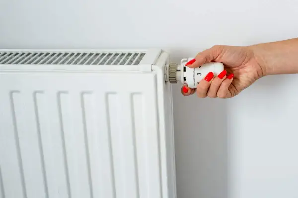 Main d'une femme aux ongles rouges tournant le thermostat pour savoir comment éteindre un radiateur électrique.