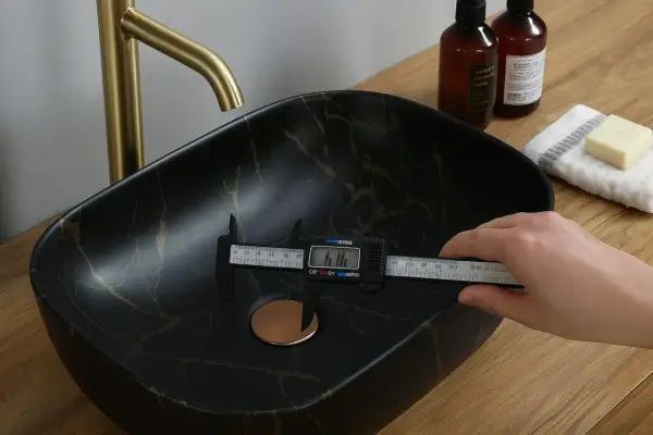Mesure du diamètre de la bonde universelle d'un lavabo noir marbré d'or.