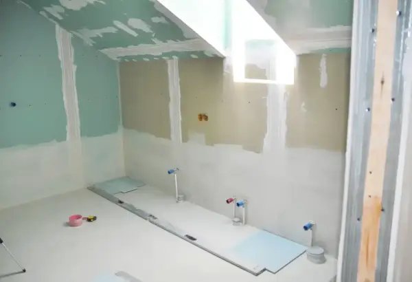 Travaux de finition dans une salle de bain : murs en plaques de plâtre, arrivées d'eau et niveau à bulle au sol. Isolation salle de bain en cours.