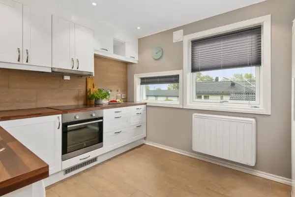 Cuisine moderne avec placards blancs, plan de travail en bois et un radiateur blanc discret assurant le chauffage.