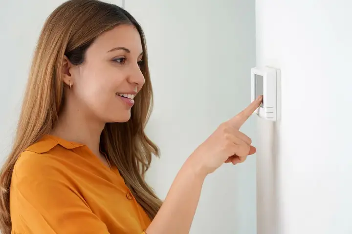 Une femme ajuste son cee thermostat connecté.