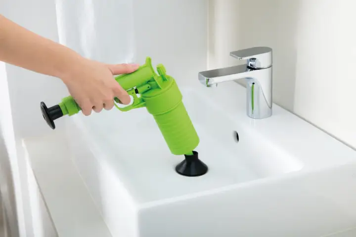 Main verte, un pistolet déboucheur est utilisé pour dégager un lavabo blanc.