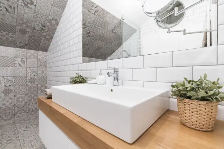 Salle de bain moderne avec lavabo rectangulaire, robinetterie chromée et un mur orné de carreaux de métro blancs et de motifs géométriques. Le **pose carrelage mural** crée un contraste saisissant.