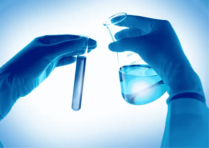 Mains gantées en laboratoire manipulant des éprouvettes et un bécher rempli d'eau.