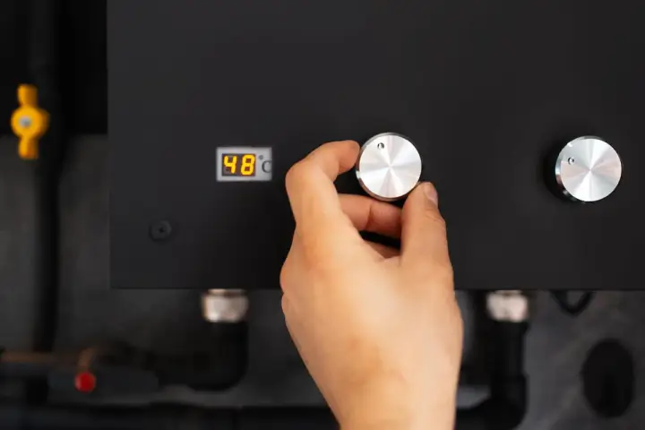 Main d'une personne ajustant le bouton d'une pompe à chaleur connectée affichant 48°C.