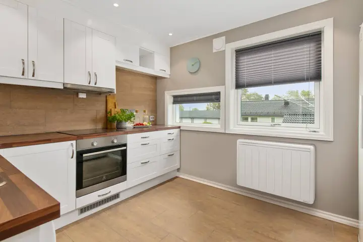 Cuisine moderne avec placards blancs, plan de travail en bois et un radiateur blanc discret assurant le chauffage.