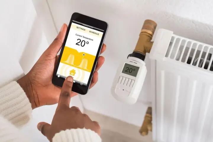 Maintenant, contrôlez votre chauffage à distance avec des solutions domotiques. Une main utilise un smartphone pour régler la température d'un radiateur.